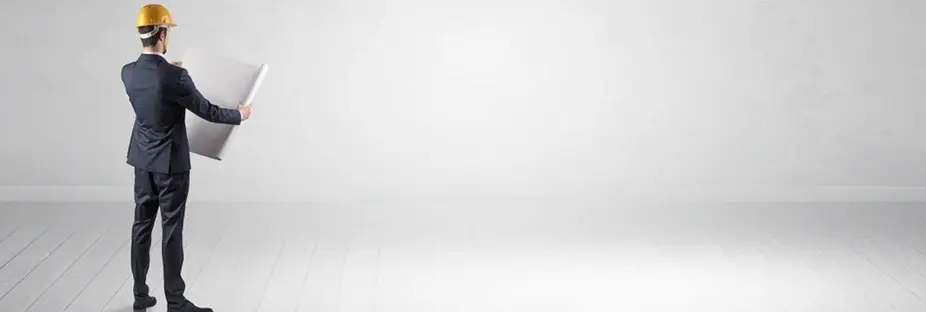 Architect with construction helmet standing in an empty space holding a plan